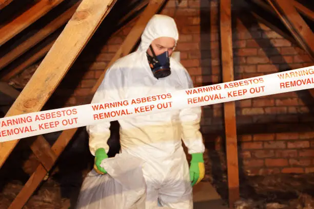 Three PPE-suited workers handling and bagging a regulated panel