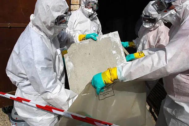 Worker in attic with WARNING ASBESTOS REMOVAL caution tape